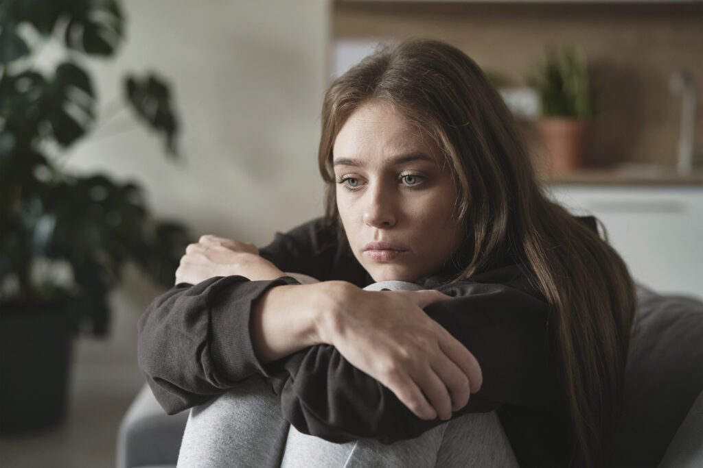 woman sitting on a sofa with hands wrapped over knees looking sad